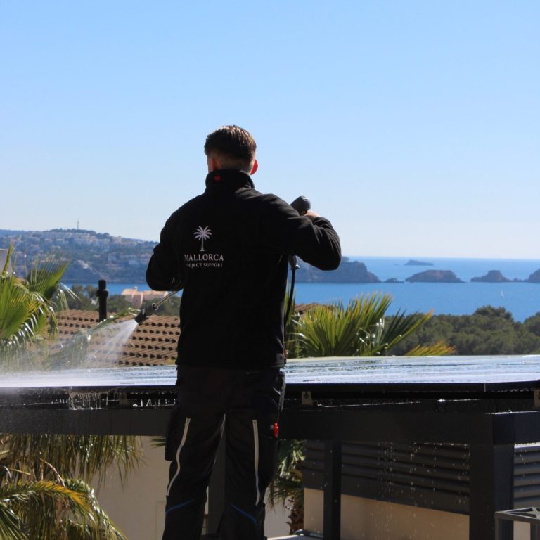 Mallorca Project Support - Deutsche Handwerker auf Mallorca Mann reinigt Solarpanele mit Blick auf das Meer und die Küste im Hintergrund.